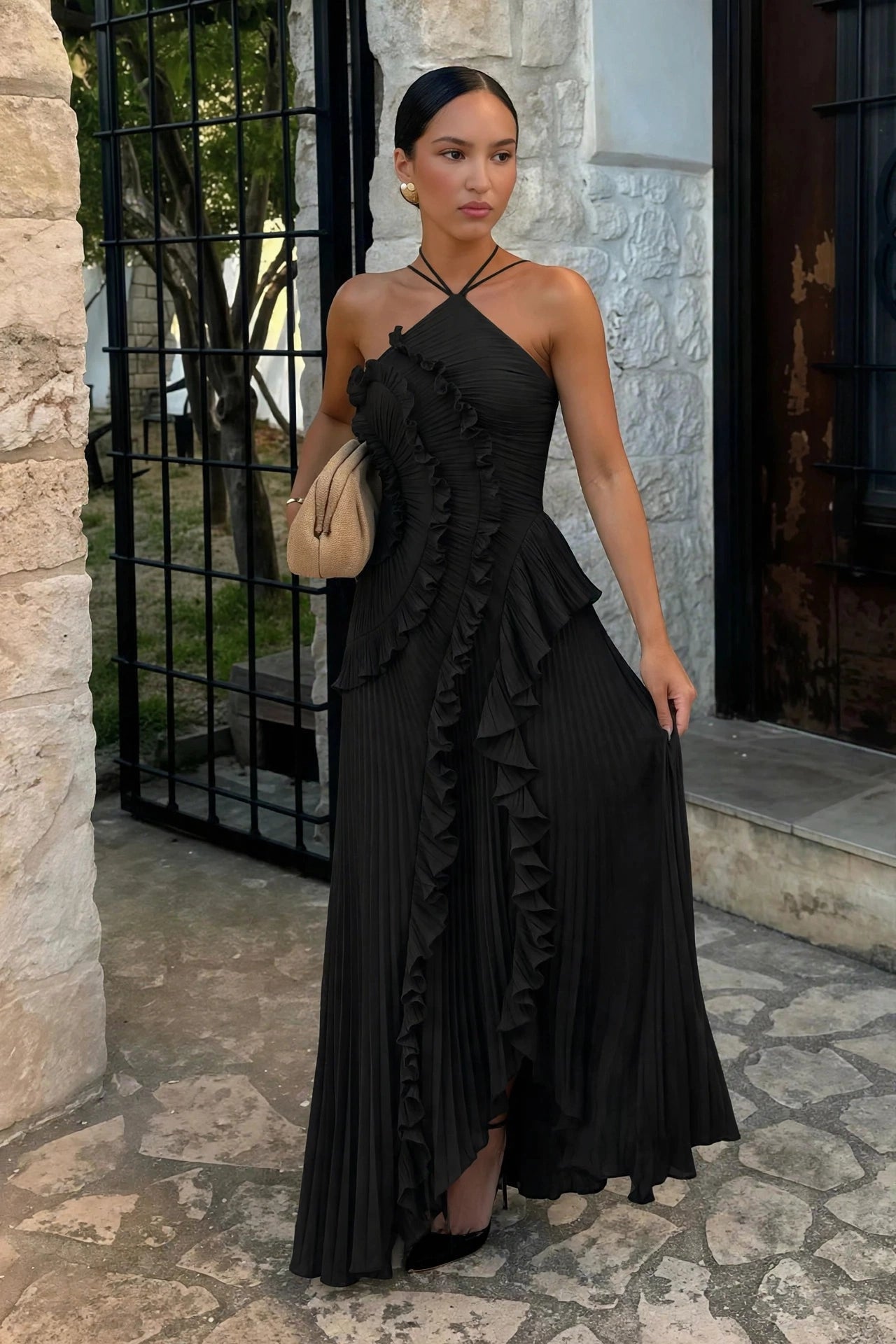 Aveline black asymmetric pleated halter ruffle maxi dress - front view, outdoor setting